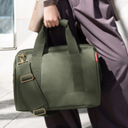 Lieblingstasche Allrounder M travel bag in olive green with gold hardware, held by a person in dark trousers.