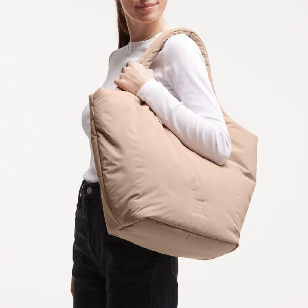 A model wearing a beige Lieblingstasche Cloud Tote Bag made from water-resistant RE:NYNET material over her shoulder.