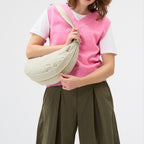 Lieblingstasche beige crescent-shaped sling bag worn by a woman in a pink sweater vest