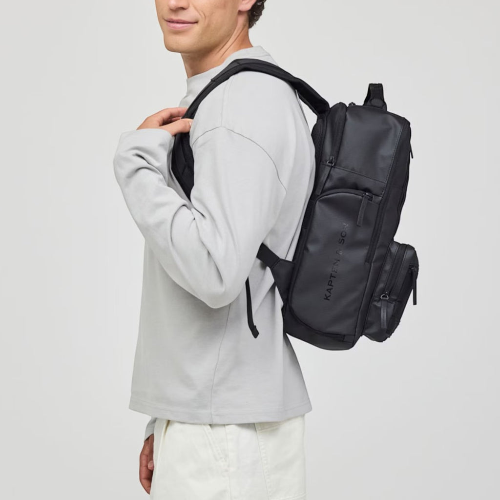 Man wearing a black Lieblingstasche Bergen Ultra backpack with a sleek, modern design against a light background.