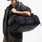 Lieblingstasche black duffle pack with multiple zippered compartments and handles, worn by a woman.