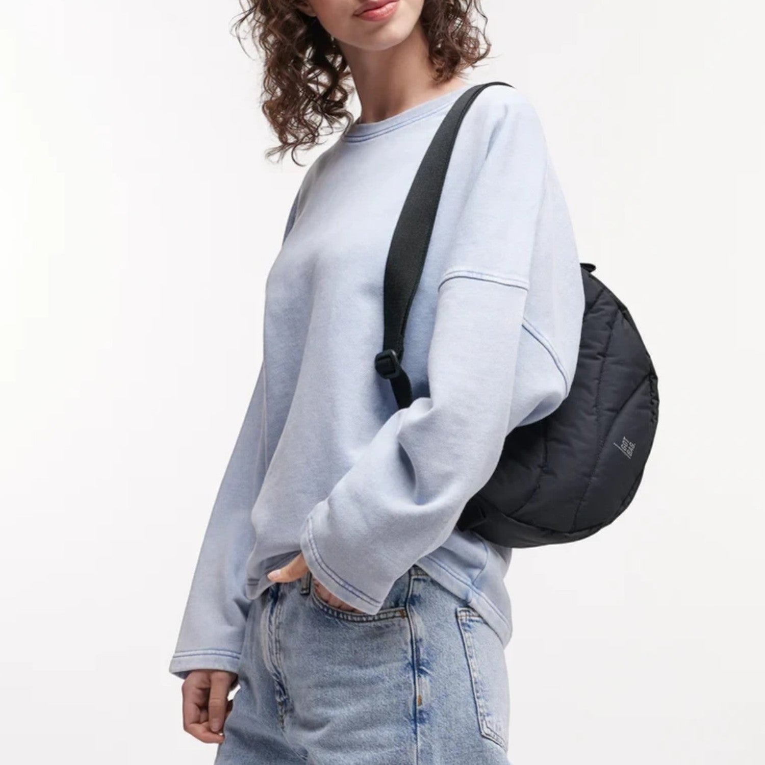 Lieblingstasche black wavy puffer moon bag worn as a crossbody by a model in a light blue sweatshirt