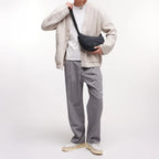 Lieblingstasche black wavy puffer moon bag worn crossbody by a man in a beige cardigan and grey trousers