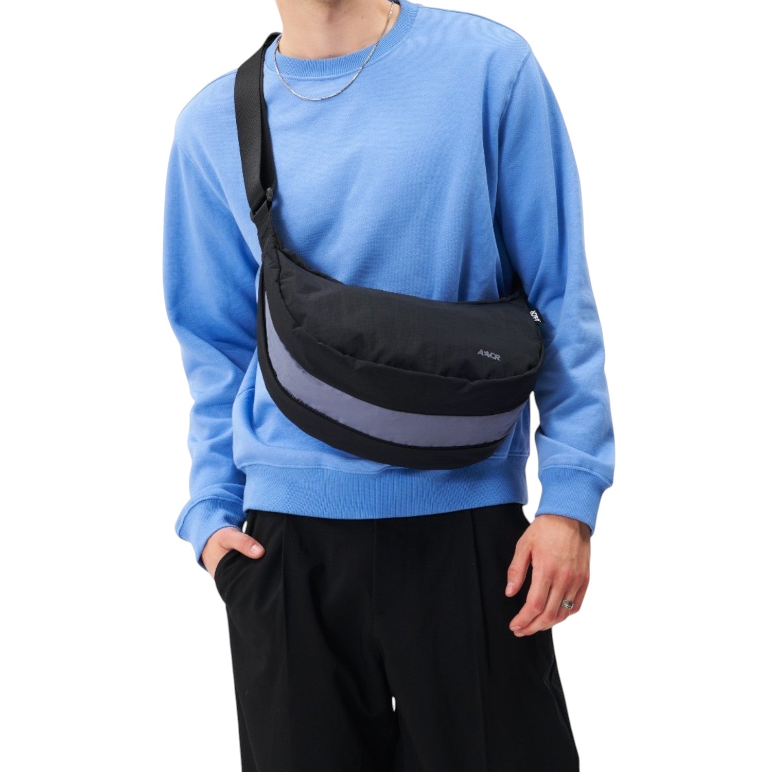 Lieblingstasche black sling bag with a grey reflective stripe worn across the chest by a man in a blue sweatshirt