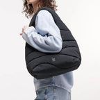 Lieblingstasche black wavy puffer shoulder bag worn by a woman in a light blue sweatshirt