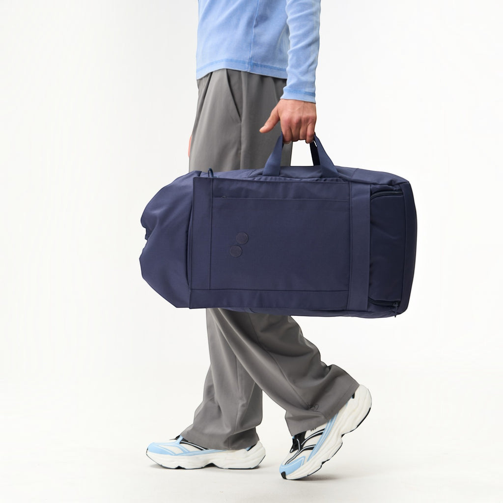Lieblingstasche Blok Large navy blue duffel bag held by a person wearing grey trousers and light blue top