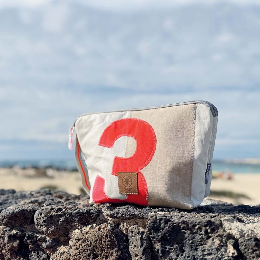 Lieblingstasche Brise pouch made from recycled sailcloth with a red number 3 design, set against a beach background.
