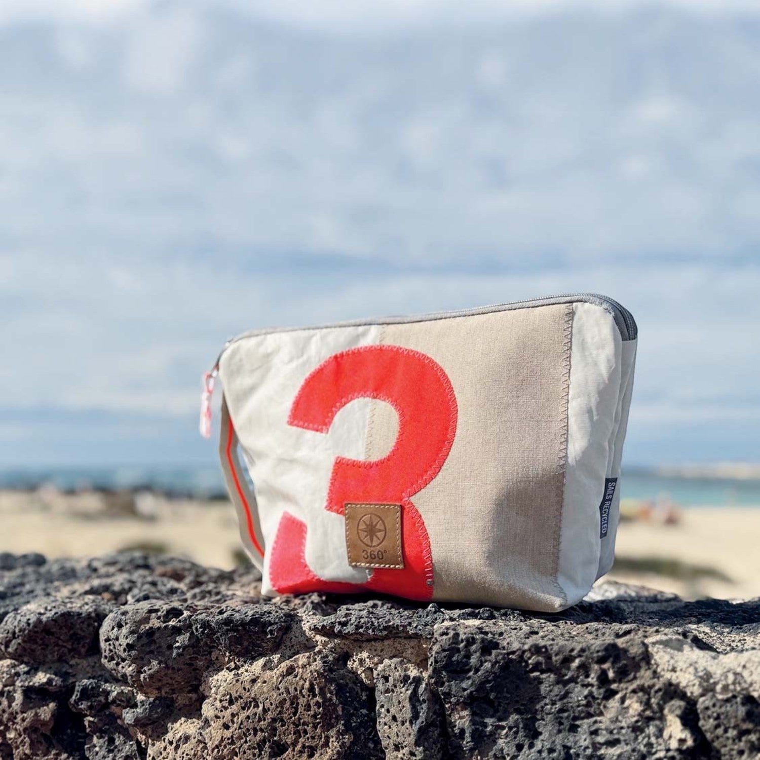 Lieblingstasche Brise pouch made from recycled sailcloth with a red number 3 design, set against a beach background.