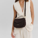 Woman wearing a dark brown suede Big Sister Suede crossbody bag by Lieblingstasche with a cream vest and trousers