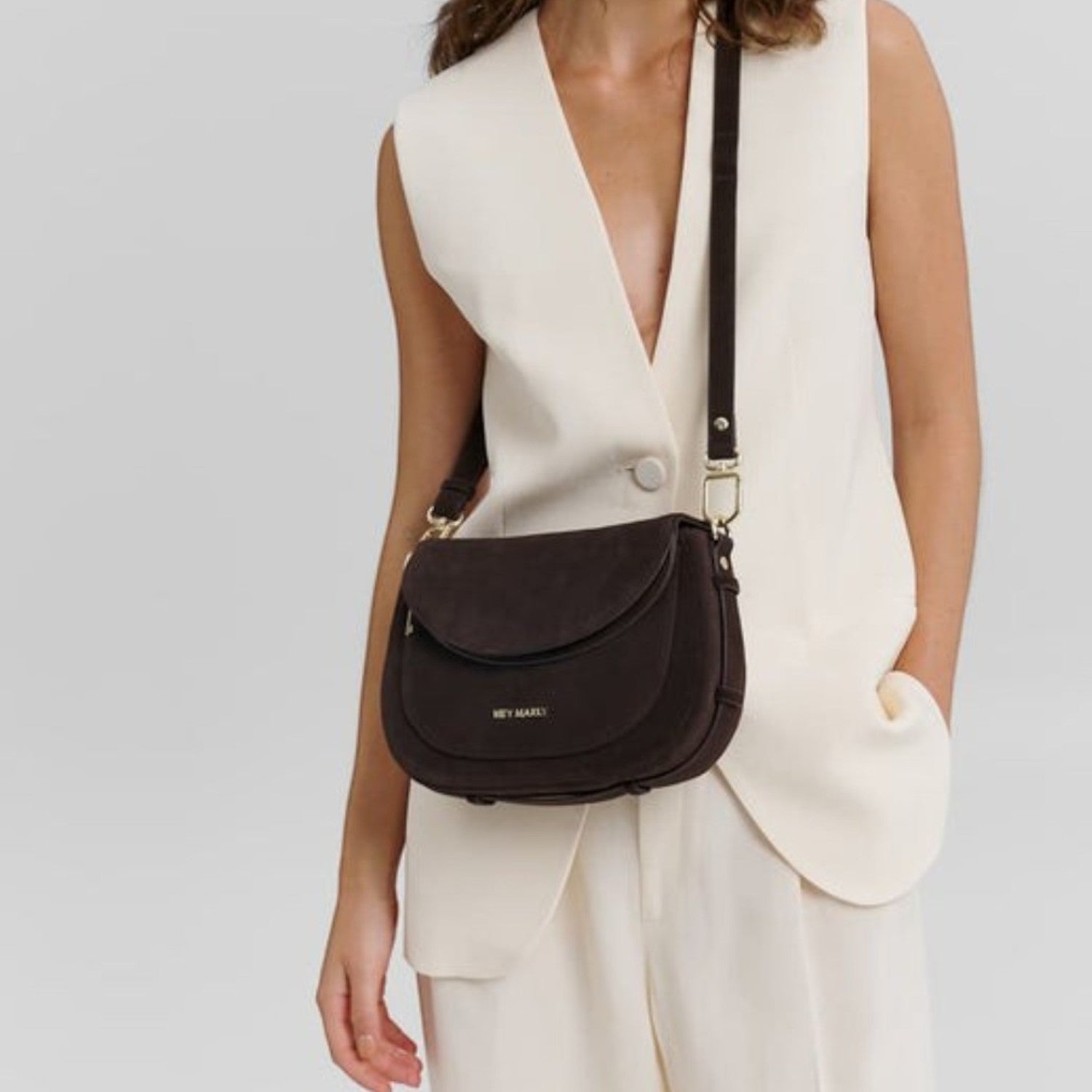 Woman wearing a dark brown suede Big Sister Suede crossbody bag by Lieblingstasche with a cream vest and trousers