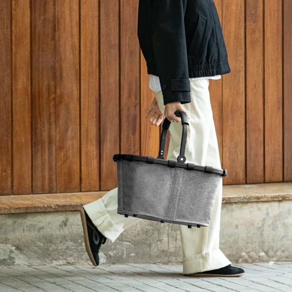 Lieblingstasche Carrybag in grey with black handle held by a woman walking in front of a wooden wall
