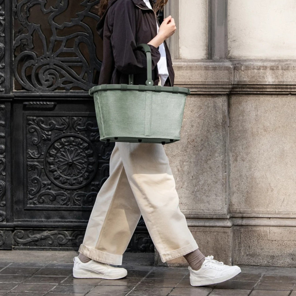 Lieblingstasche Carrybag in sage green with a soft-grip handle, carried by a woman walking on a city street.