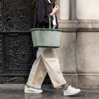 Lieblingstasche Carrybag in sage green with a soft-grip handle, carried by a woman walking on a city street.