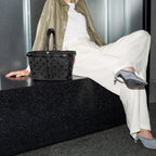 Lieblingstasche Carrybag XS in black with a subtle polka dot pattern, held by a woman in a modern studio setting.