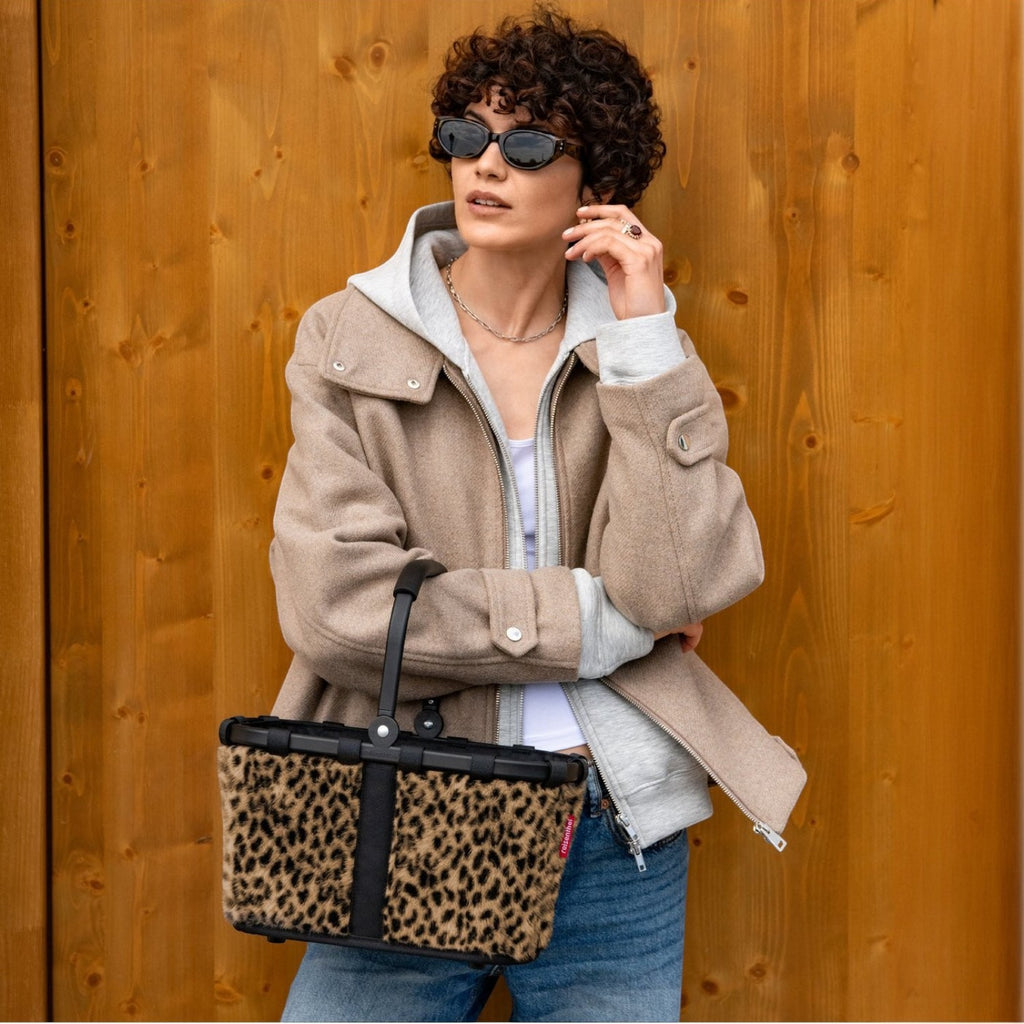 Lieblingstasche Carrybag XS with a leopard print pattern, black frame, and handle held by a woman in a beige jacket.