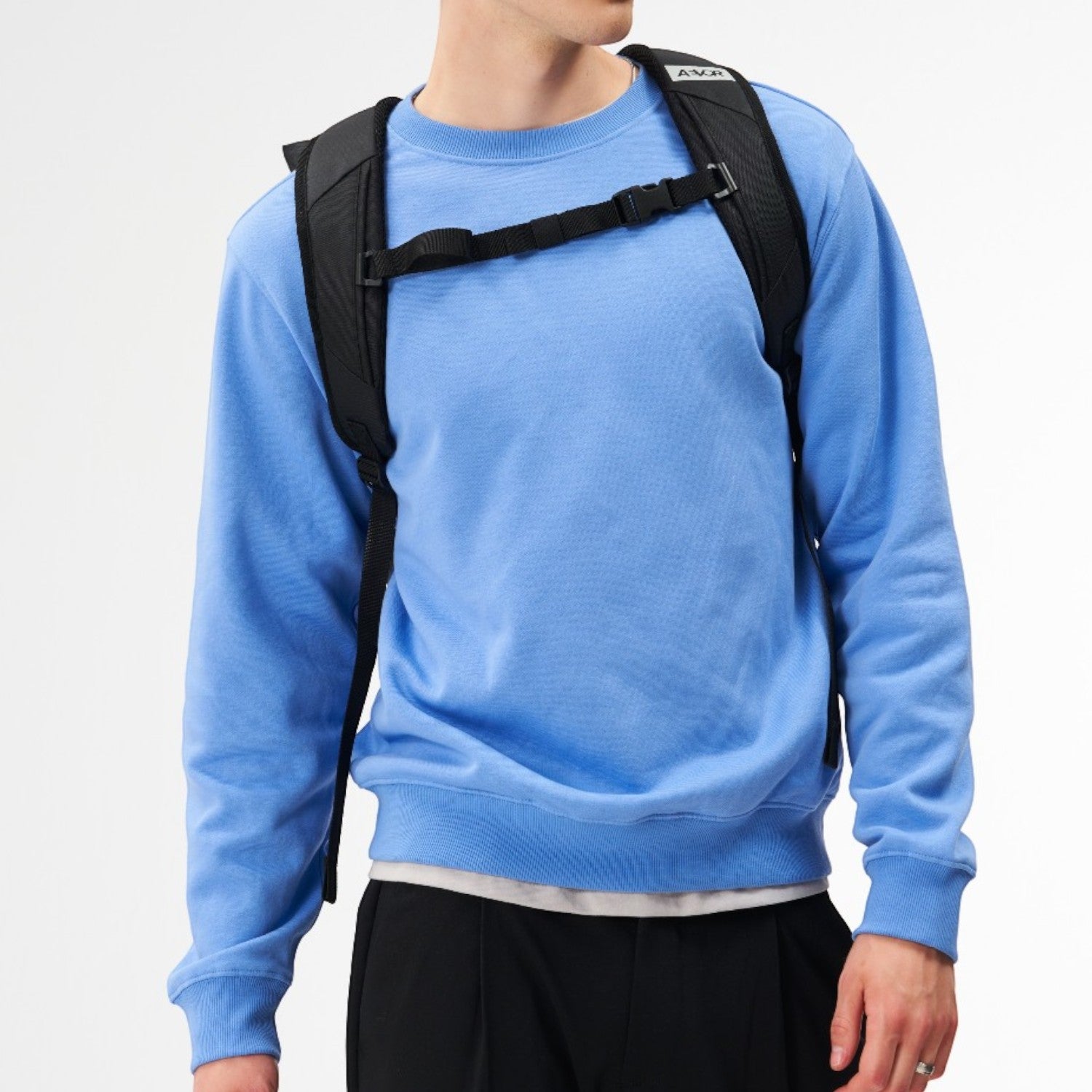A man wearing a black Lieblingstasche Day Pack FLX backpack with adjustable chest straps against a white background.