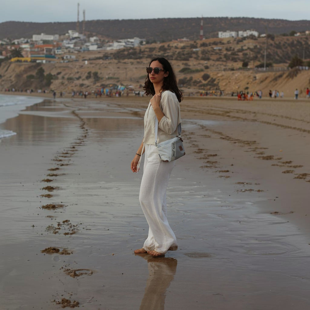 Woman wearing a Lieblingstasche Deern Lütt crossbody bag on a sandy beach at sunset