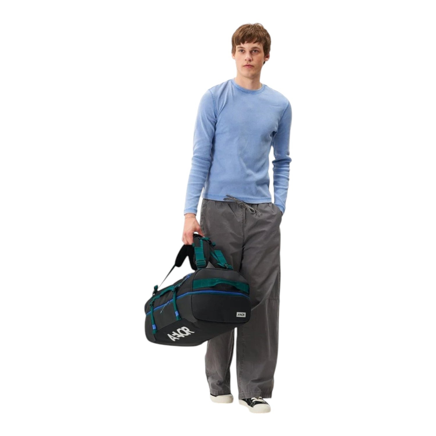 Lieblingstasche Duffel Pack in black with green accents, held by a model wearing a light blue shirt and grey trousers.