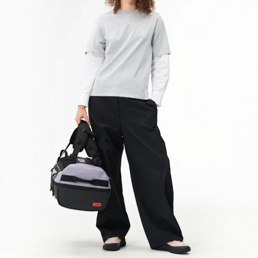 Lieblingstasche Duffel Pack in grey and black, held by a model wearing a grey t-shirt and black trousers.