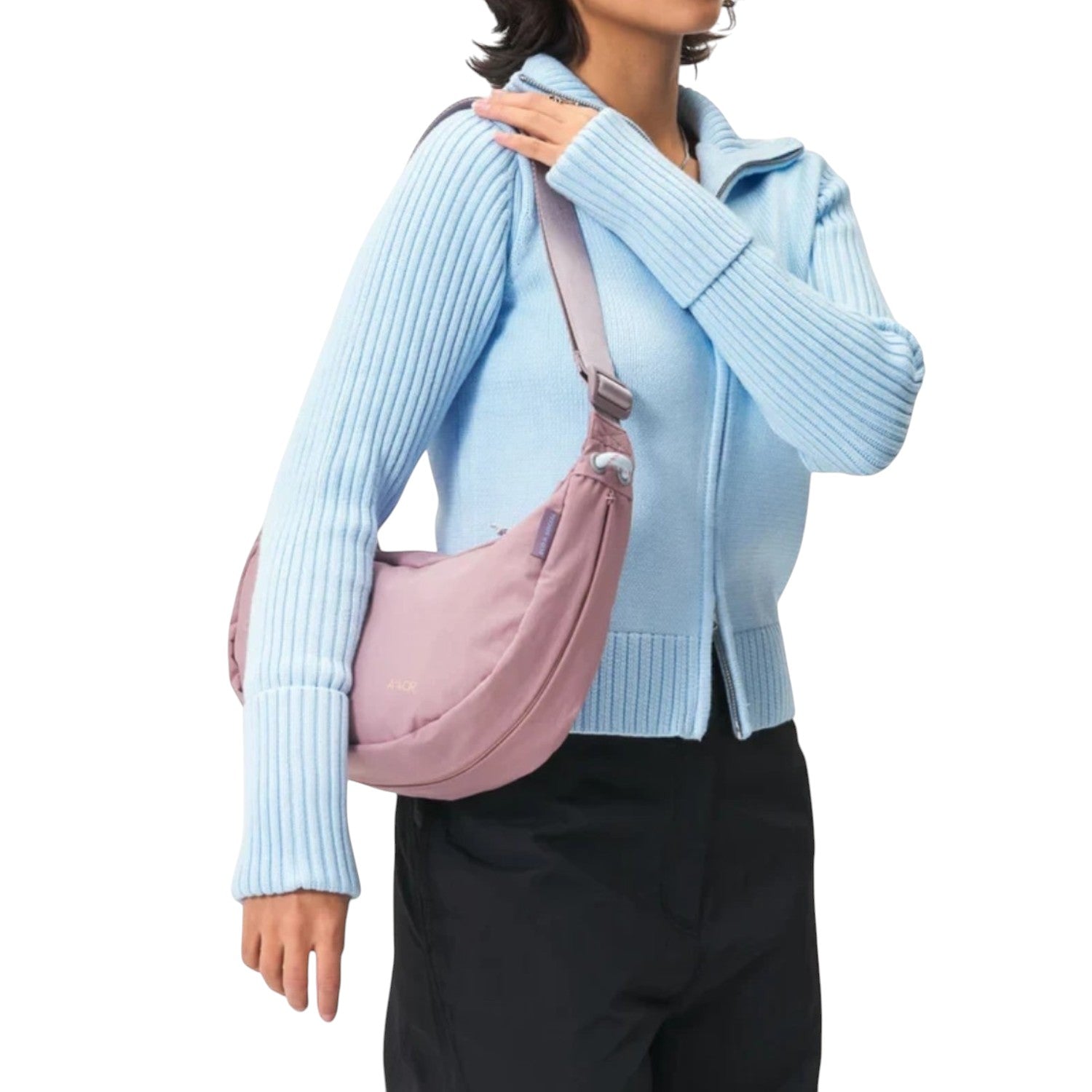 A model wearing a Lieblingstasche dusty pink crescent-shaped sling bag over a light blue ribbed zip-up sweater.