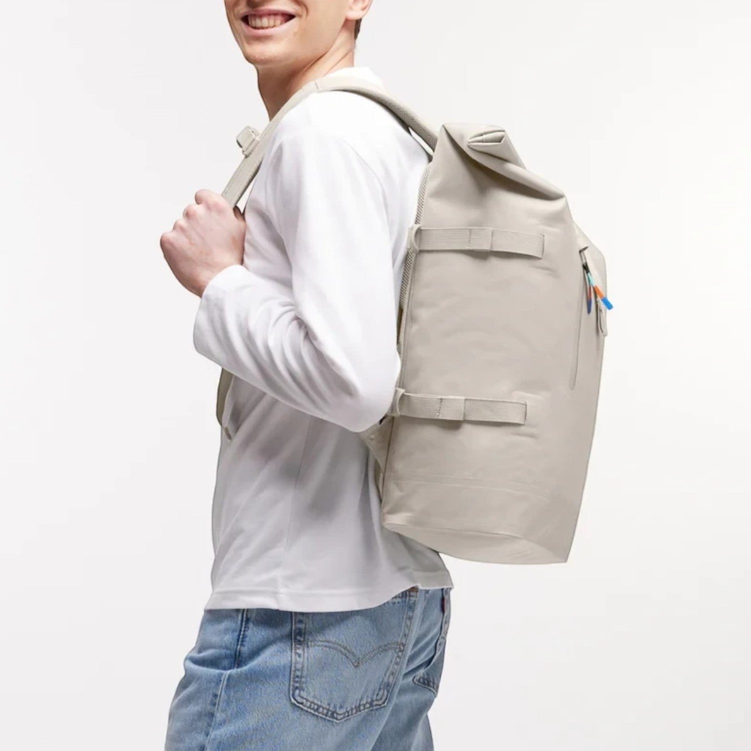 Man wearing a beige Lieblingstasche GOT BAG Rolltop 2.0 backpack with adjustable straps against a white background