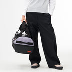 Model holding a Lieblingstasche grey and black duffel pack with adjustable straps against a white background