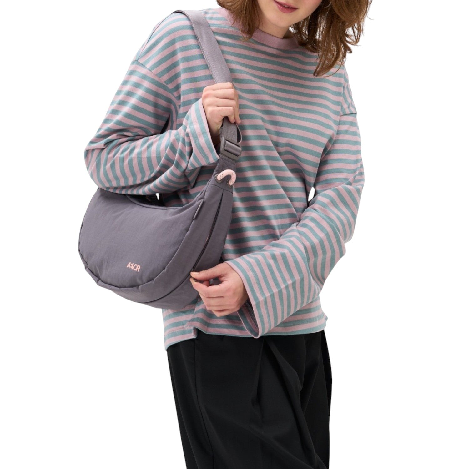 Lieblingstasche grey crescent-shaped sling bag worn over the shoulder by a woman in a striped long-sleeve shirt.