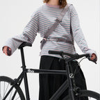 Lieblingstasche grey sling bag worn across the chest by a woman in a striped long-sleeve shirt with a black bicycle
