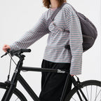 Lieblingstasche slouchy grey crossbody bag worn by a woman in a striped long-sleeve shirt riding a black bicycle