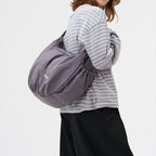 Lieblingstasche slouchy bag in grey worn over the shoulder by a woman in a striped long-sleeve shirt