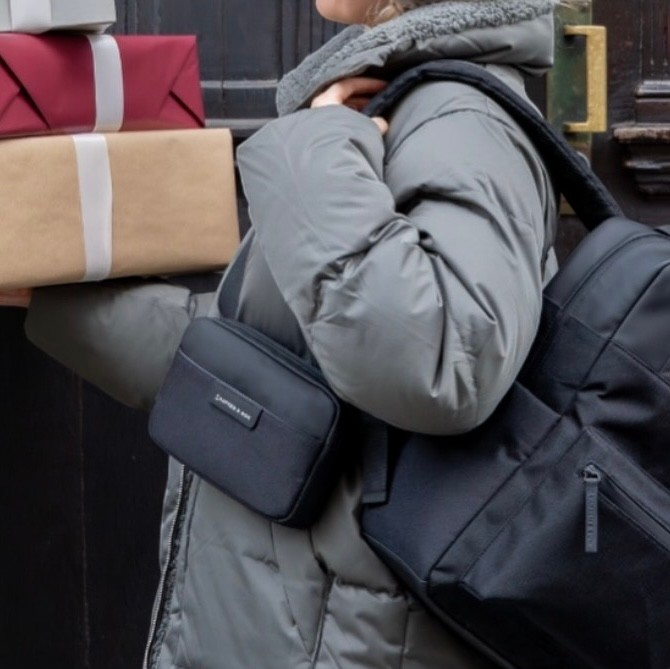 Lieblingstasche Habo black crossbody bag worn by a person in a grey puffer jacket holding gift boxes