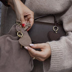 Lieblingstasche heart charm accessory attached to a taupe suede handbag held by a woman in a beige sweater