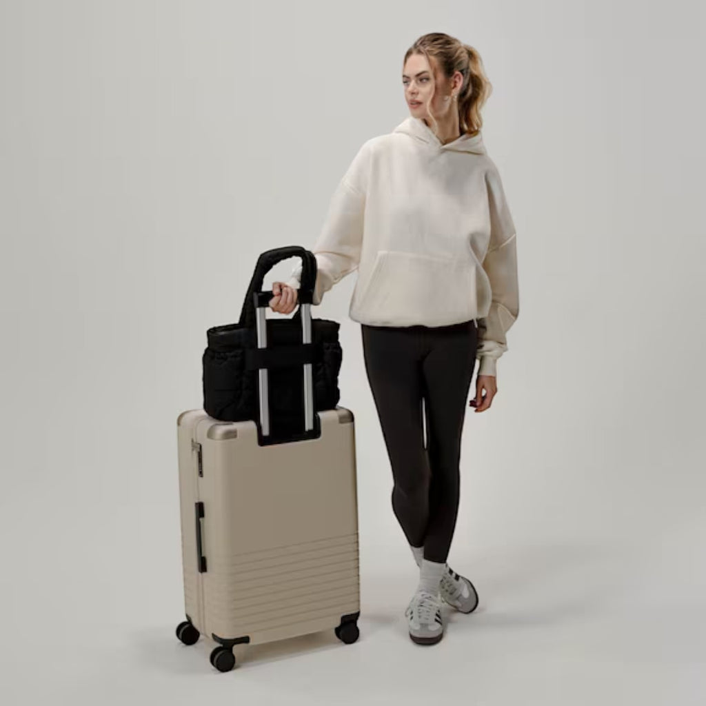 Lieblingstasche Hellvi Cloud Medium black quilted bag attached to a beige suitcase, held by a woman in casual wear.