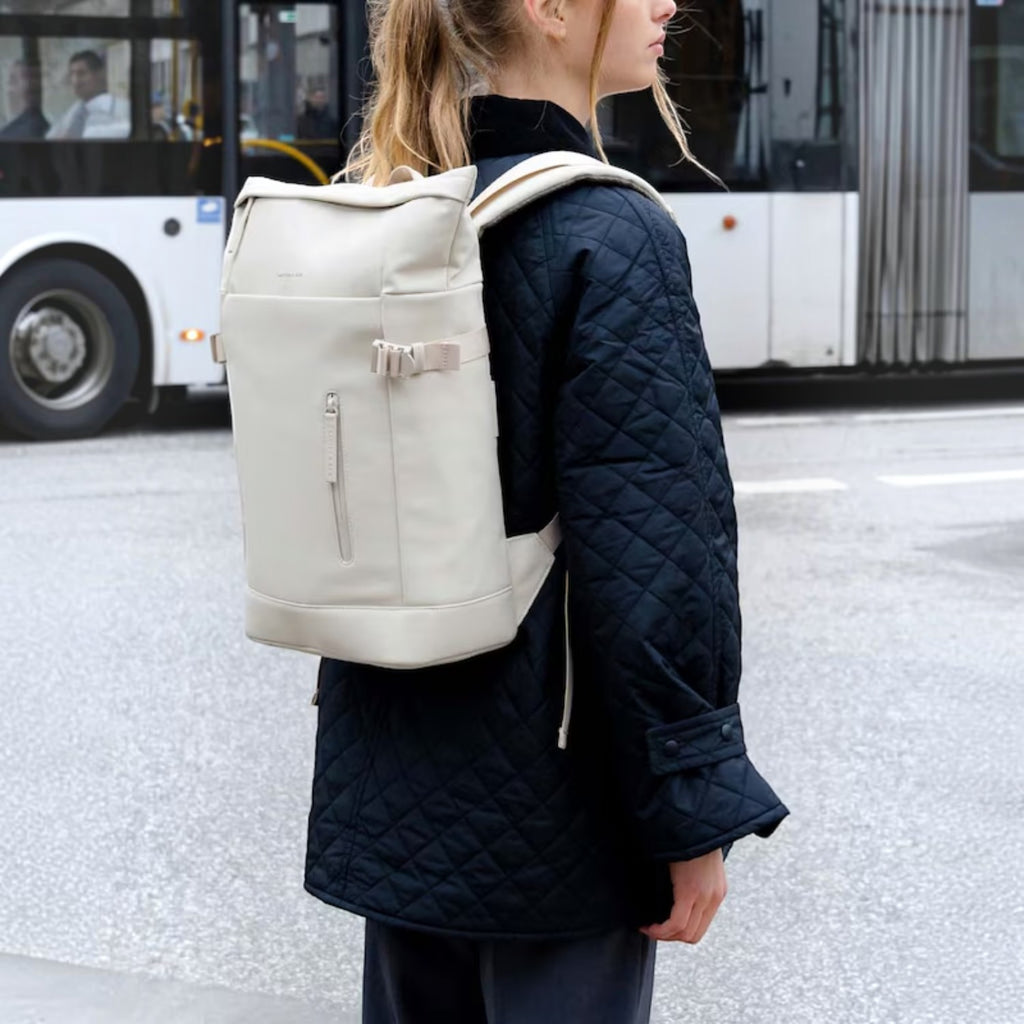 Lieblingstasche Helsinki backpack in off-white with a roll-top design, worn by a woman in a black quilted jacket.