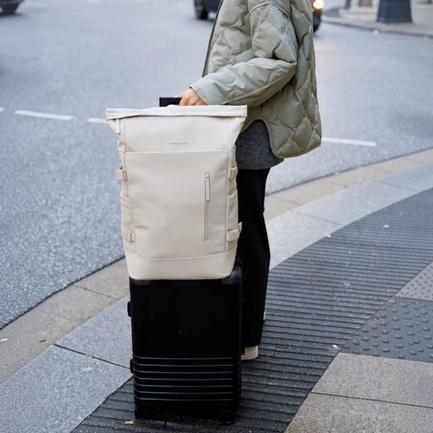 Lieblingstasche Helsinki Pro beige rolltop backpack resting on a black suitcase on a city street