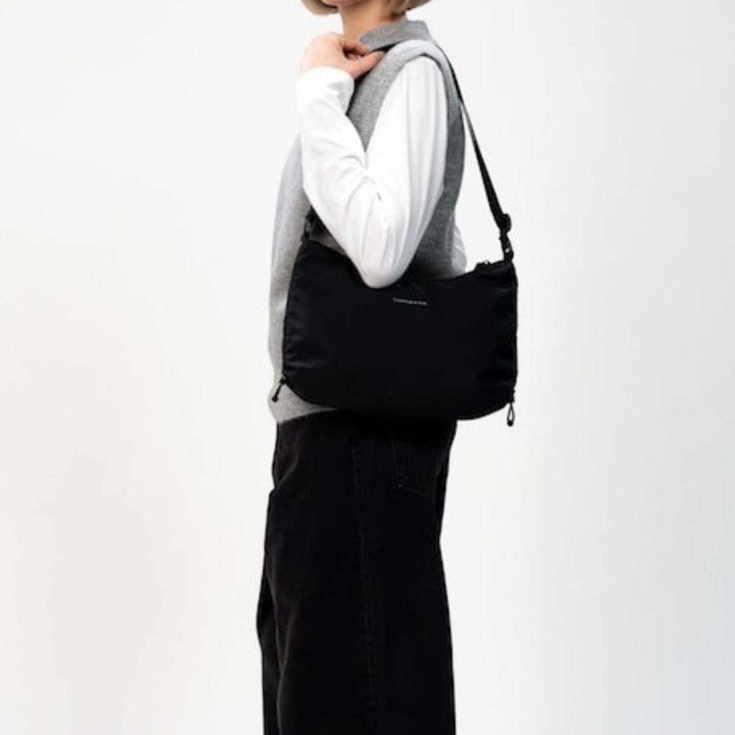 Lieblingstasche Kapten & Son Skara Small black shoulder bag worn by a woman in a grey vest and white long-sleeve top.