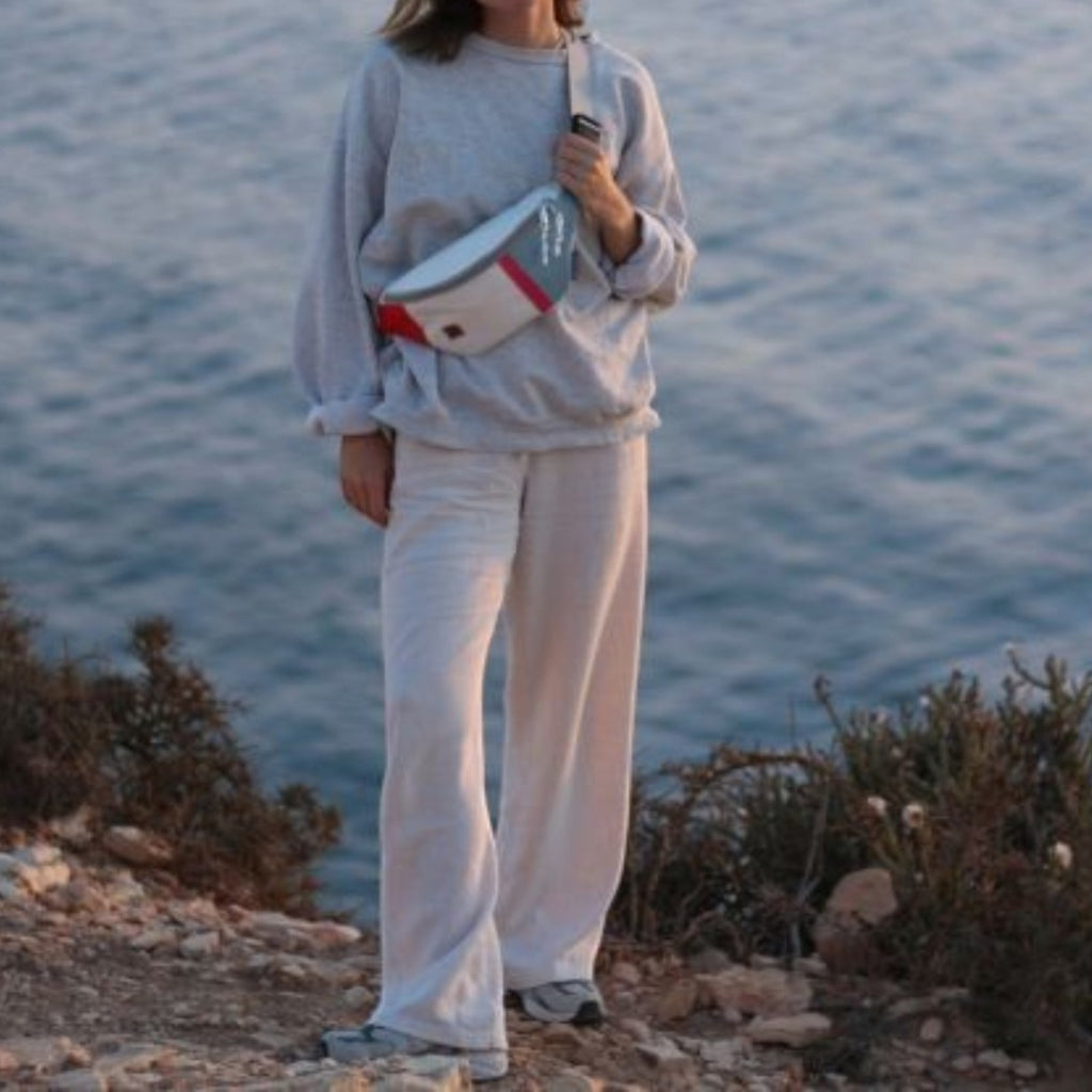 Lieblingstasche Knoten belt bag made from recycled sailcloth with red and grey accents worn by a woman by the sea