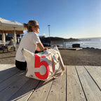 Lieblingstasche Kutter XL sailcloth bag with a large red number 5, resting on a wooden deck by the ocean.