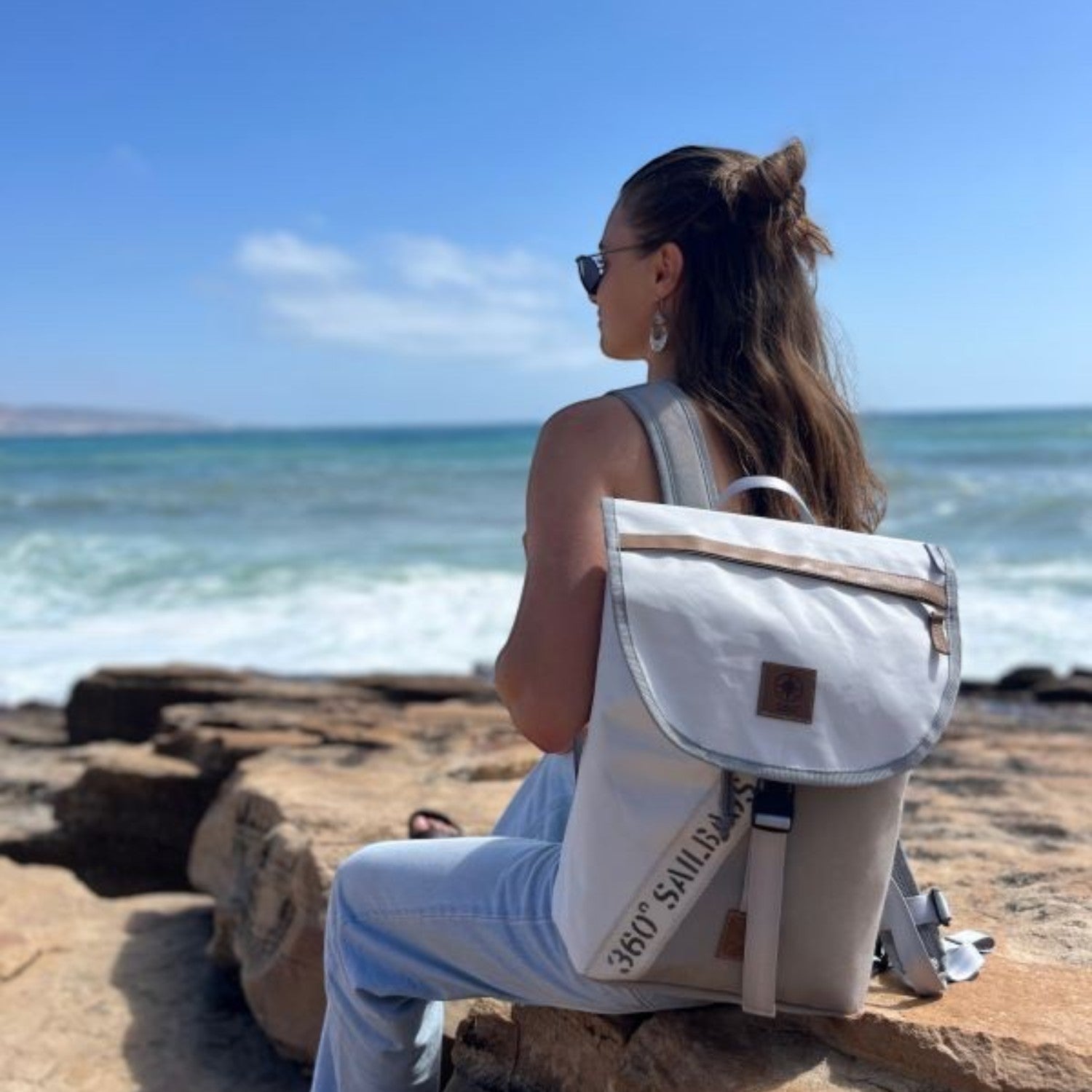Lieblingstasche Landgang Mini backpack made from recycled white sailcloth worn by a woman sitting by the ocean