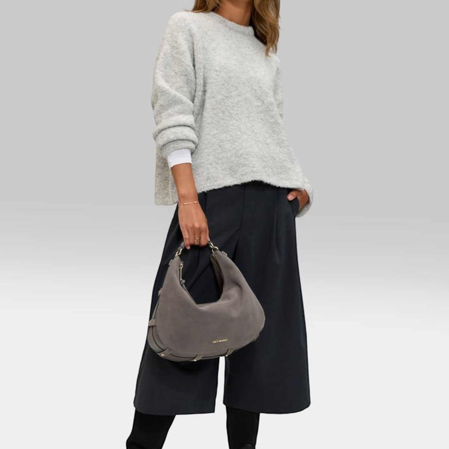 Lieblingstasche Lifetime Sister Suede M grey suede hobo bag held by a model wearing a grey sweater and black culottes