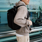 Man wearing a black Lieblingstasche Lisbon Pro travel backpack with ergonomic straps in a modern airport setting