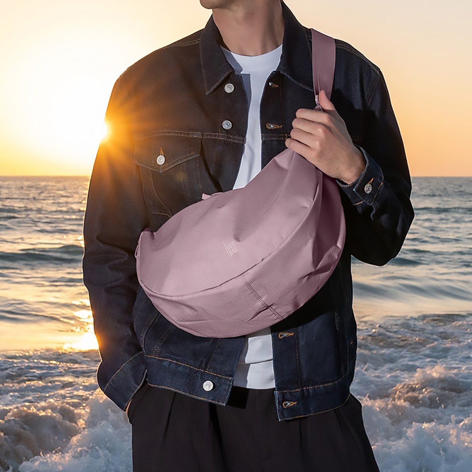 Lieblingstasche Large Moon Bag in dusty rose, worn crossbody by a man on a beach at sunset.