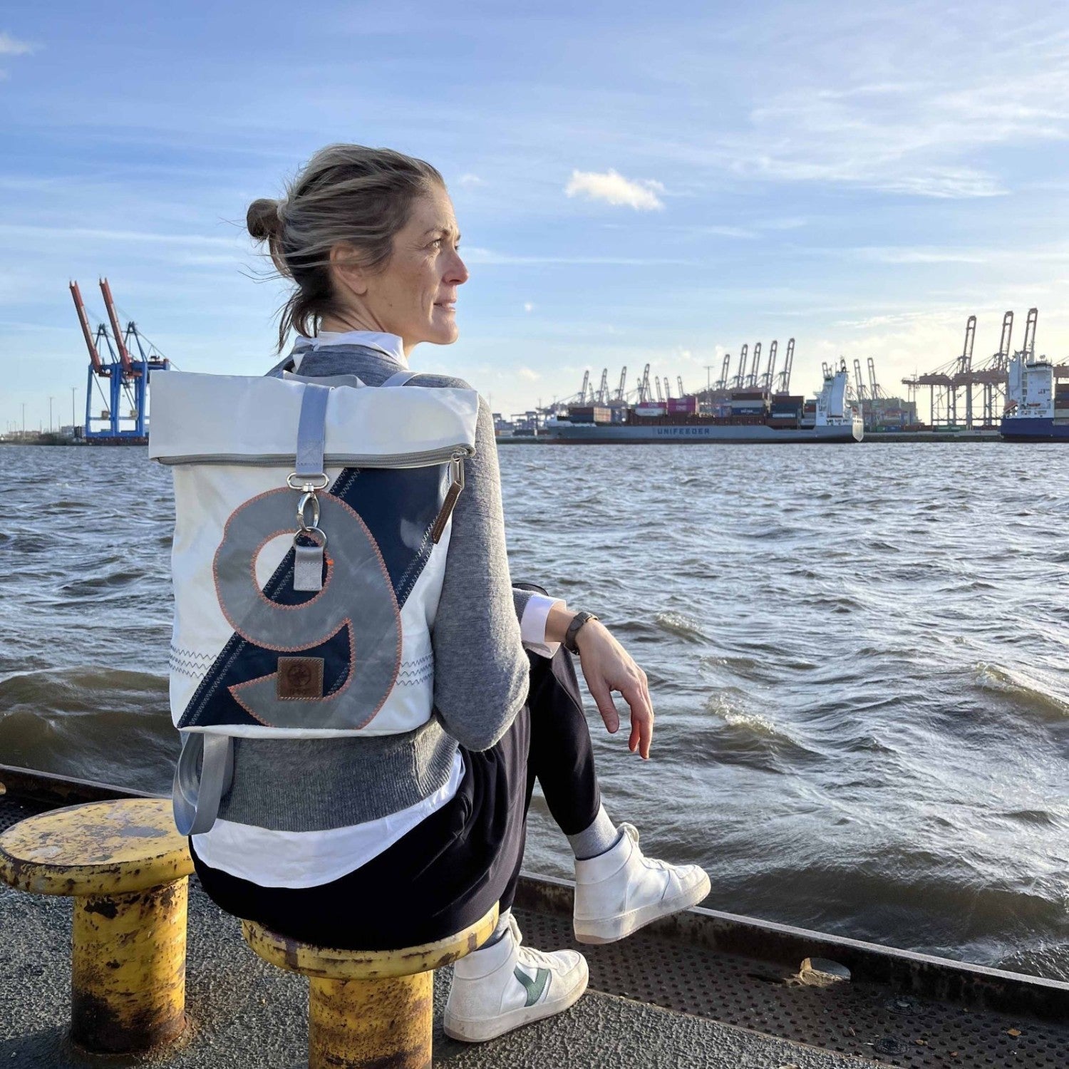 Lieblingstasche Möwe backpack with roll-top closure and number 9 design, worn by a woman at the harbor.