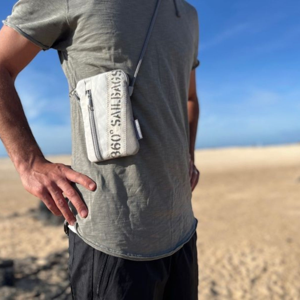 Lieblingstasche Nautik Lütt crossbody phone bag made of white recycled sailcloth with unique stitching on a beach