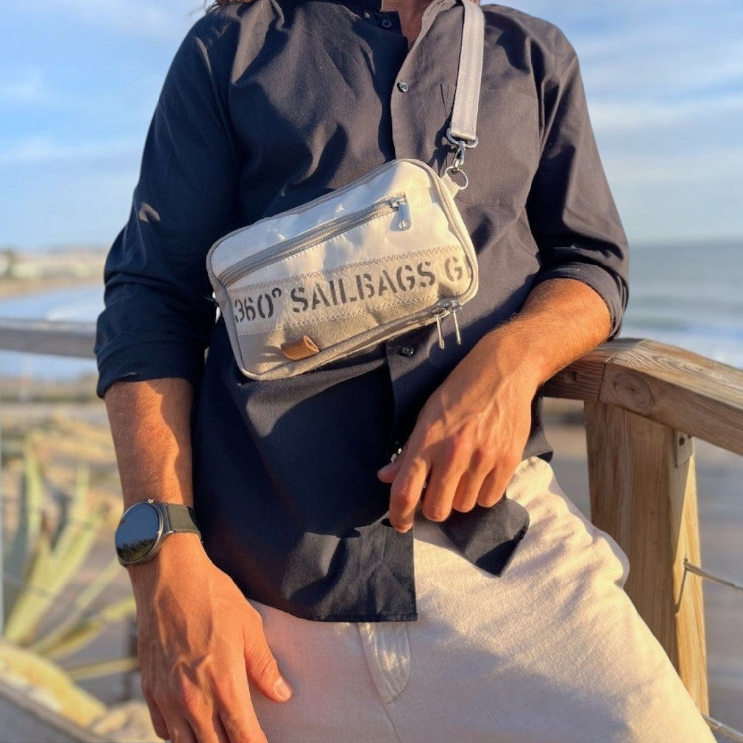 Lieblingstasche Nautik crossbody bag in white sailcloth worn by a man on a coastal boardwalk at sunset