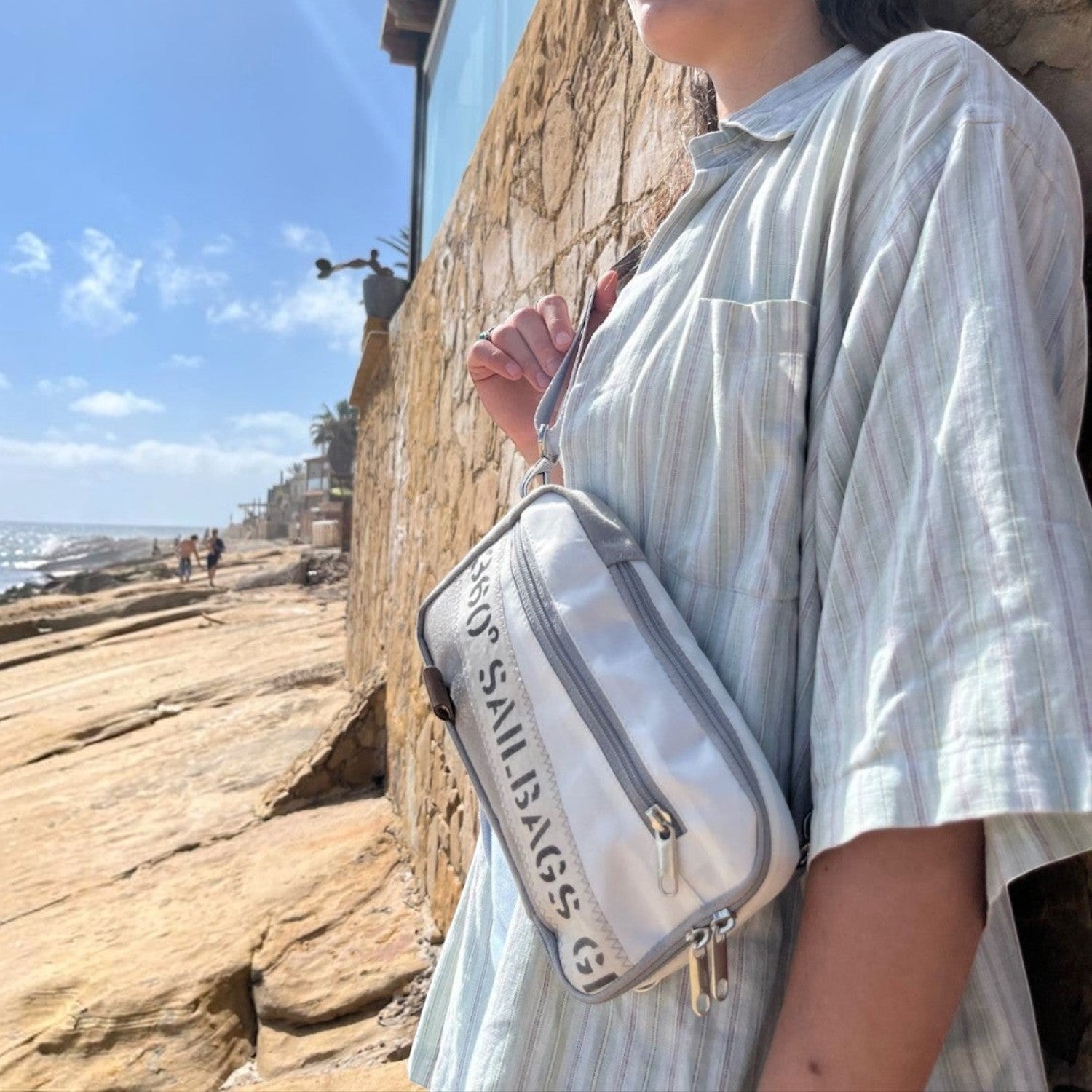 Lieblingstasche Nautik white sailcloth crossbody bag worn by a woman against a stone wall by the ocean