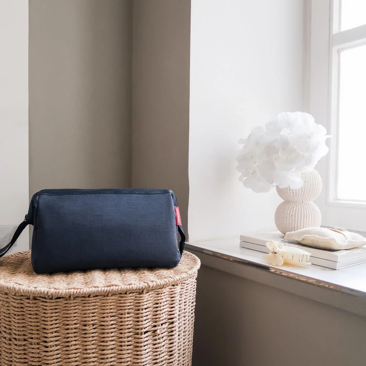 Lieblingstasche Travelcosmetic navy blue toiletry bag sitting on a wicker basket near a bright window