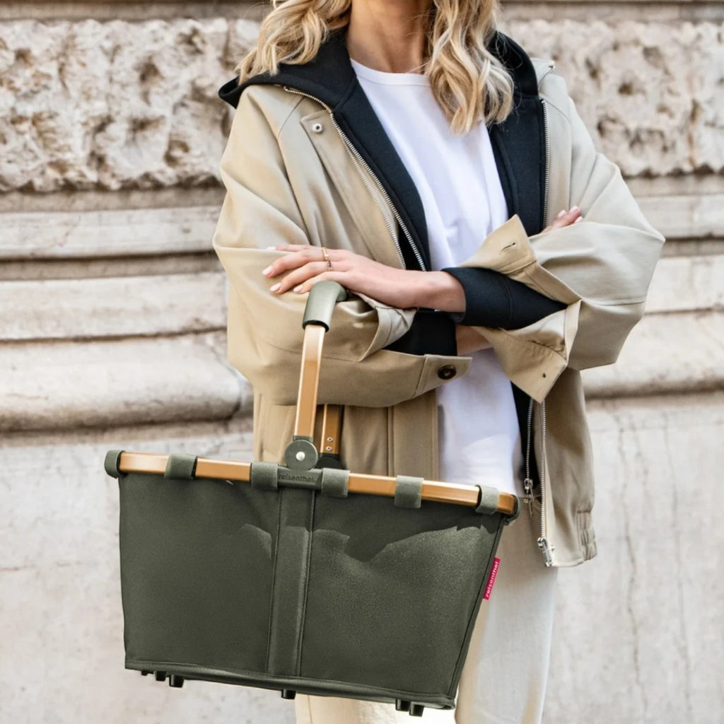Lieblingstasche carrybag in olive green with a sturdy aluminium handle, held by a woman in a beige jacket.