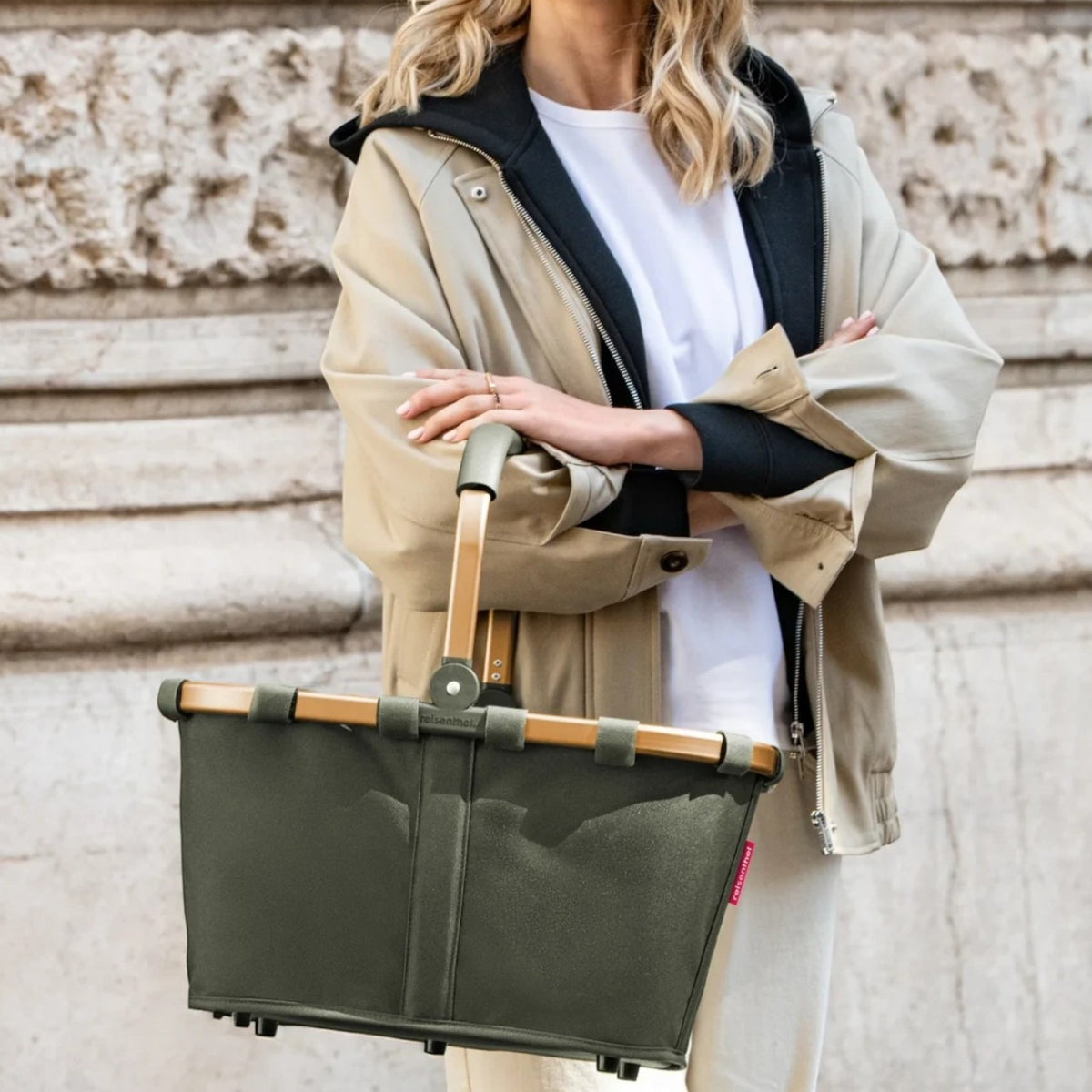 Lieblingstasche carrybag in olive green with a sturdy aluminium handle, held by a woman in a beige jacket.