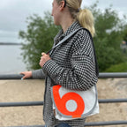 Lieblingstasche Perle white messenger bag with a bold orange circular logo worn over the shoulder by a woman